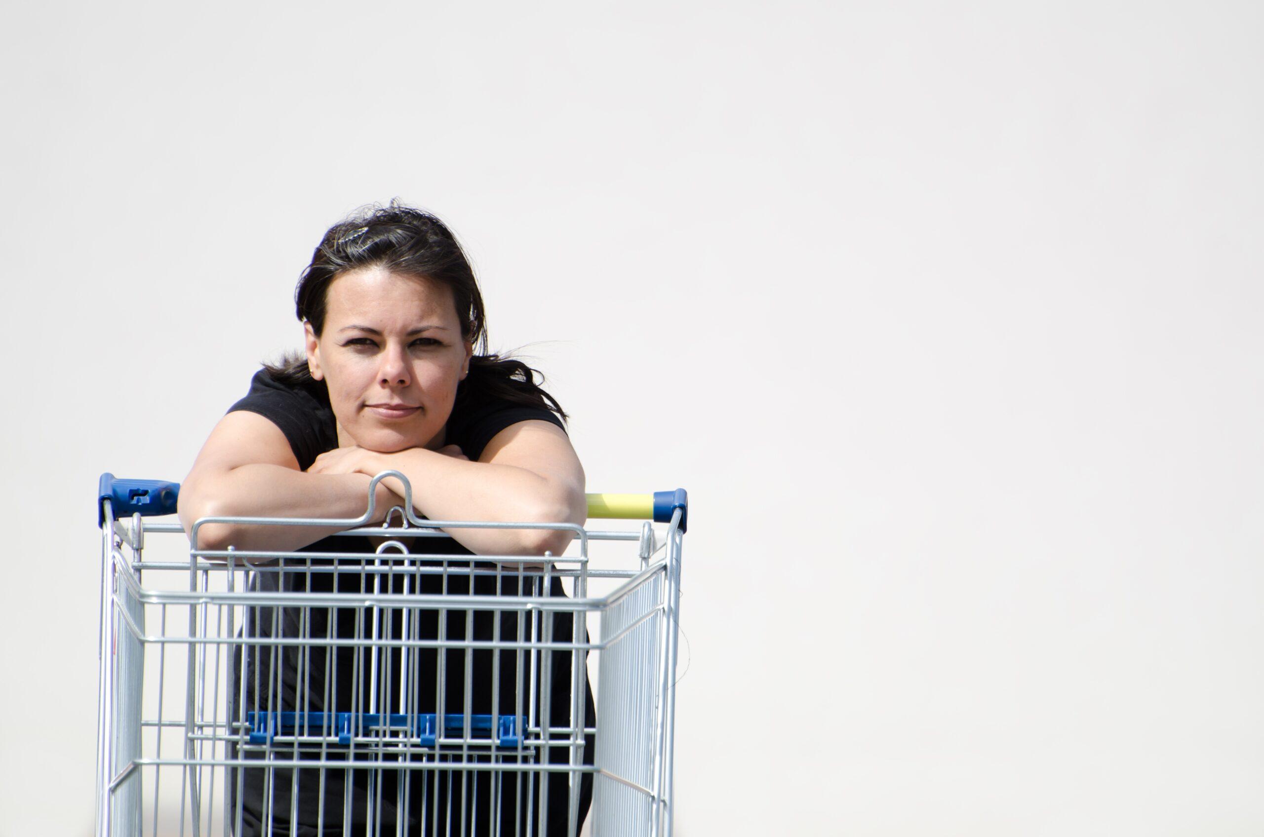 Female wearing a black shirt leaning on a shopping cart with a white background