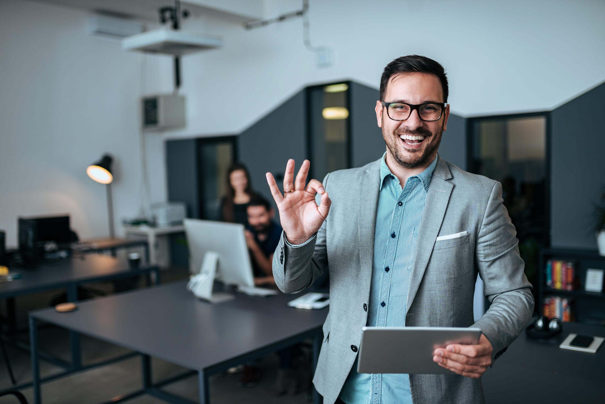 Handsome young businessman showing OK gesture in modern office.